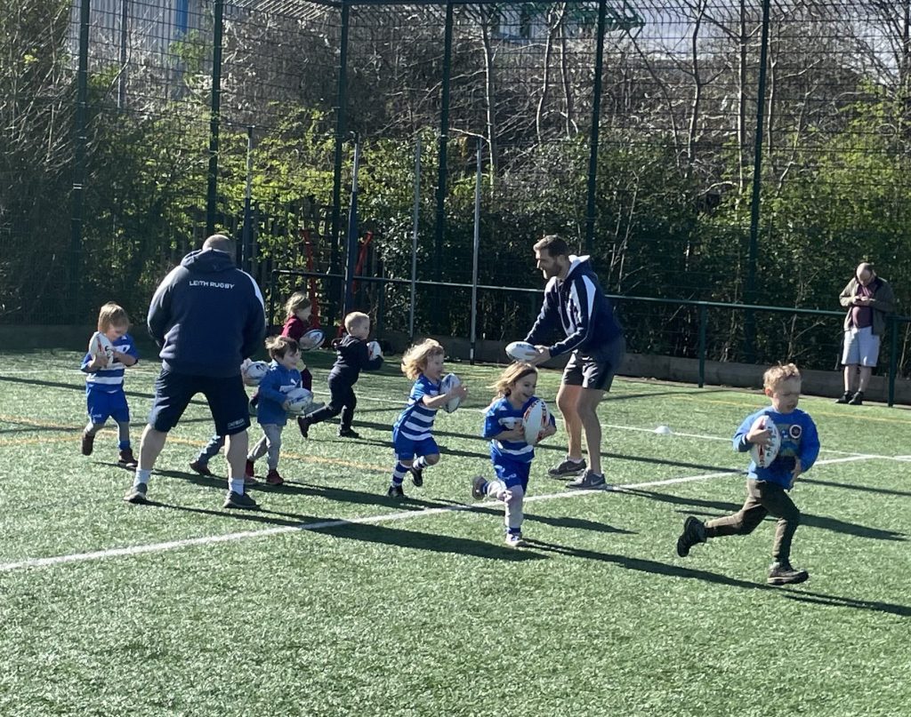 Young children playing rugby in blue and white striped shirts